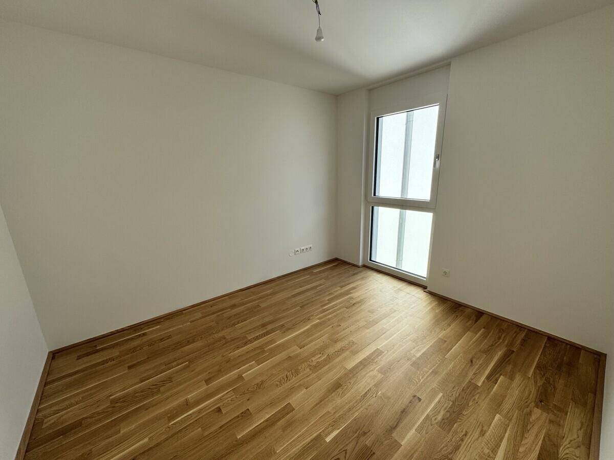 Unmöbliertes Zimmer mit Holzboden und einem hohen Fenster, ideal als Schlaf- oder Arbeitszimmer.