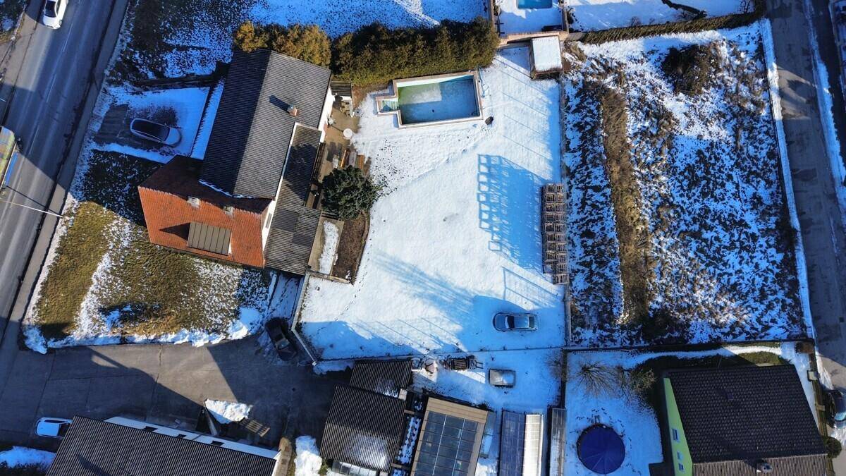 Draufsicht auf das Grundstück mit Wohnhaus, Gartenbereich und Swimmingpool im Schnee.