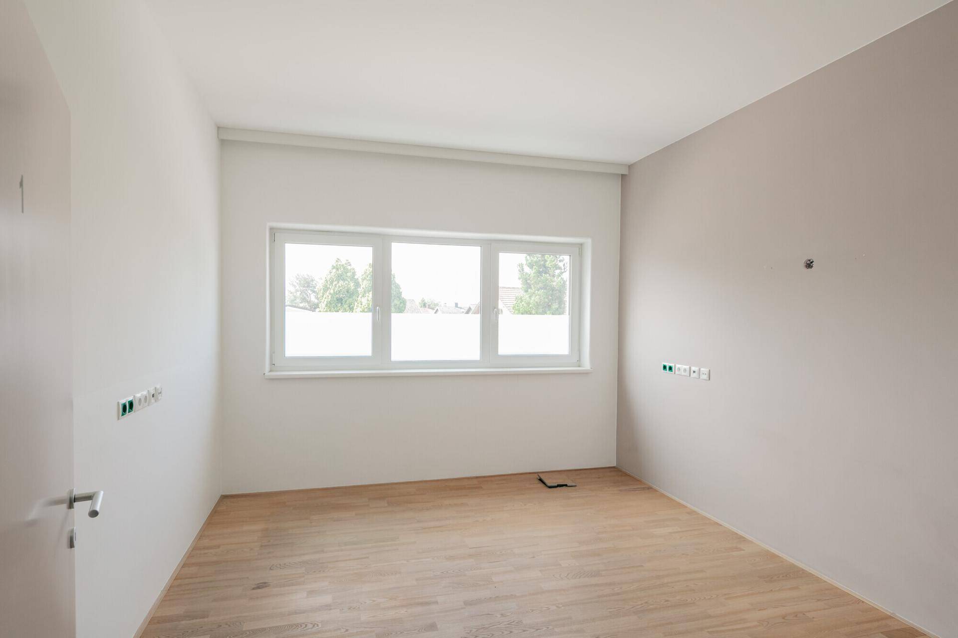Heller Büroraum mit Holzfußboden und Fenster, vorbereitet für die Installation von Technik und Möbeln.