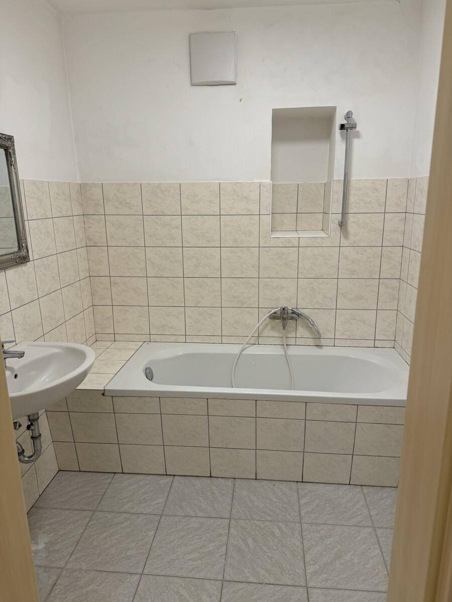 Badezimmer mit Badewanne, Waschbecken und hellen Fliesen an Wänden und Boden.