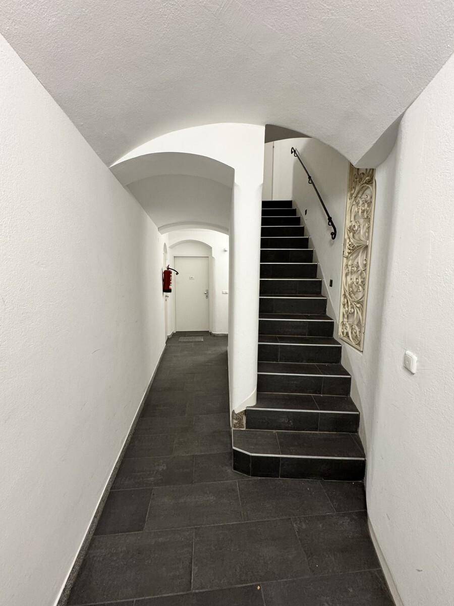 Langer Flur mit dunklen Fliesen und gewölbter Decke, der zu einer Treppe führt.