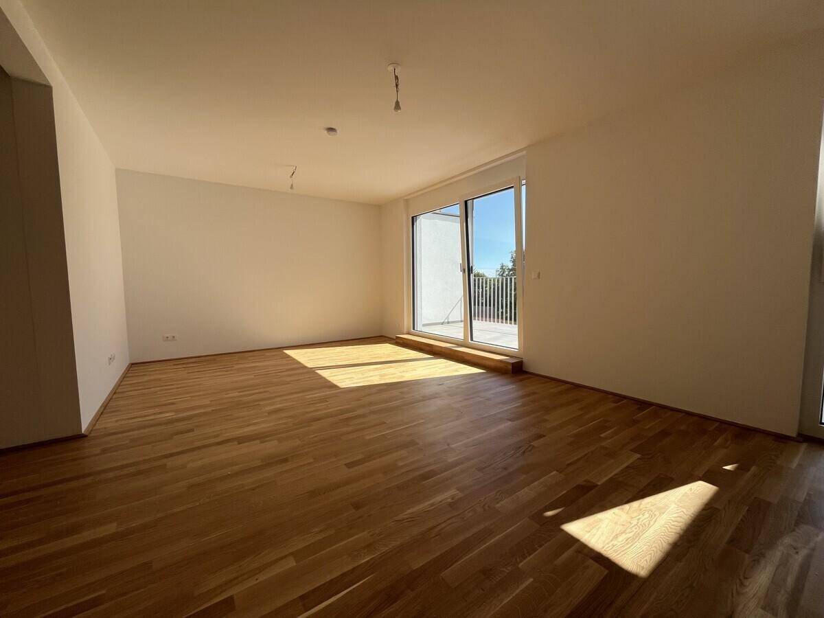 Geräumiges Wohnzimmer mit Holzboden und großen Fenstern, die viel Tageslicht hereinlassen.