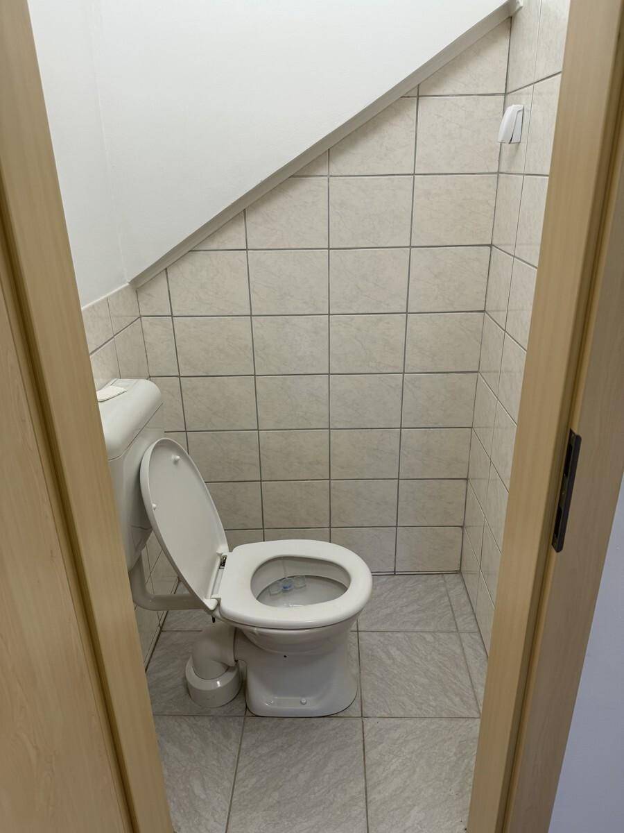 Separate Toilette mit hellen Fliesen und einem Fenster unter der Dachschräge.