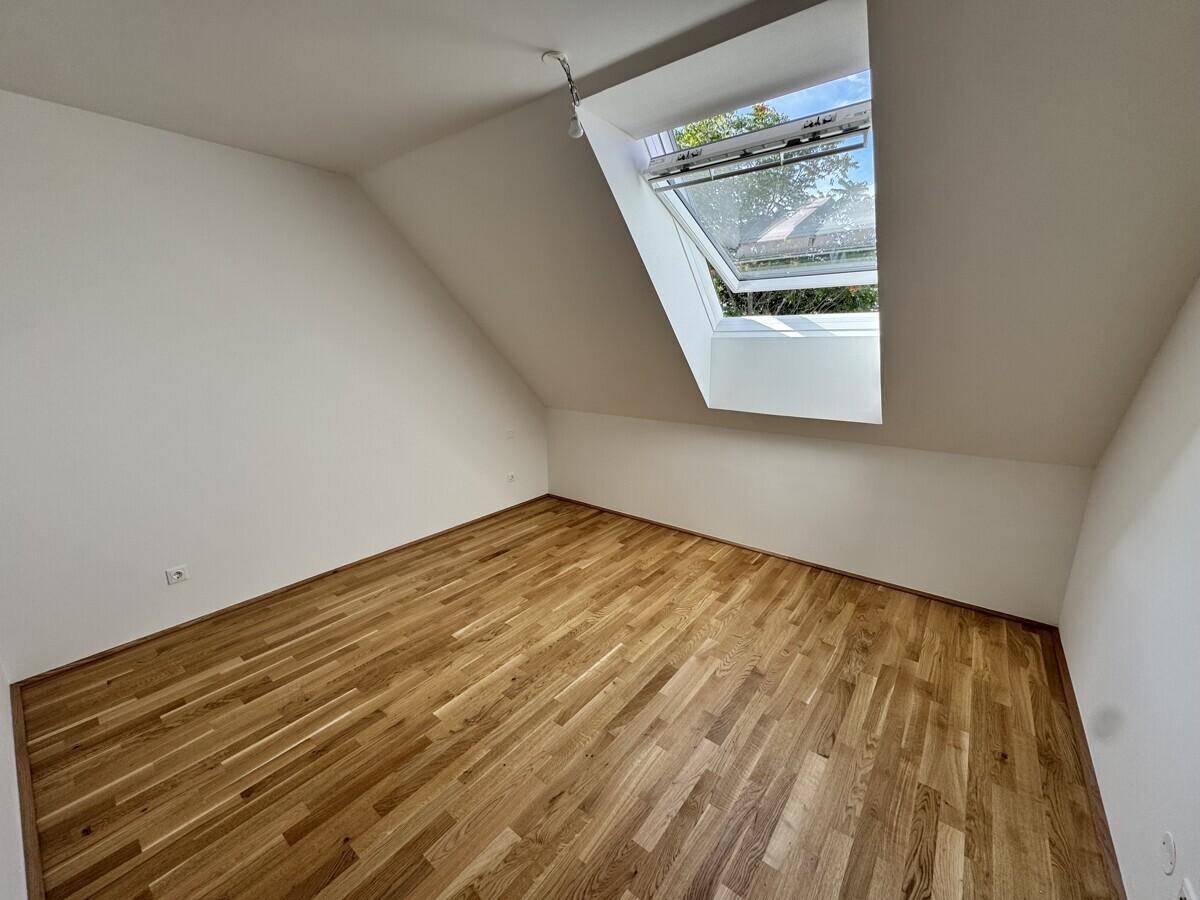 Dachzimmer mit Holzboden und einem großen Dachfenster, das viel natürliches Licht hereinlässt.