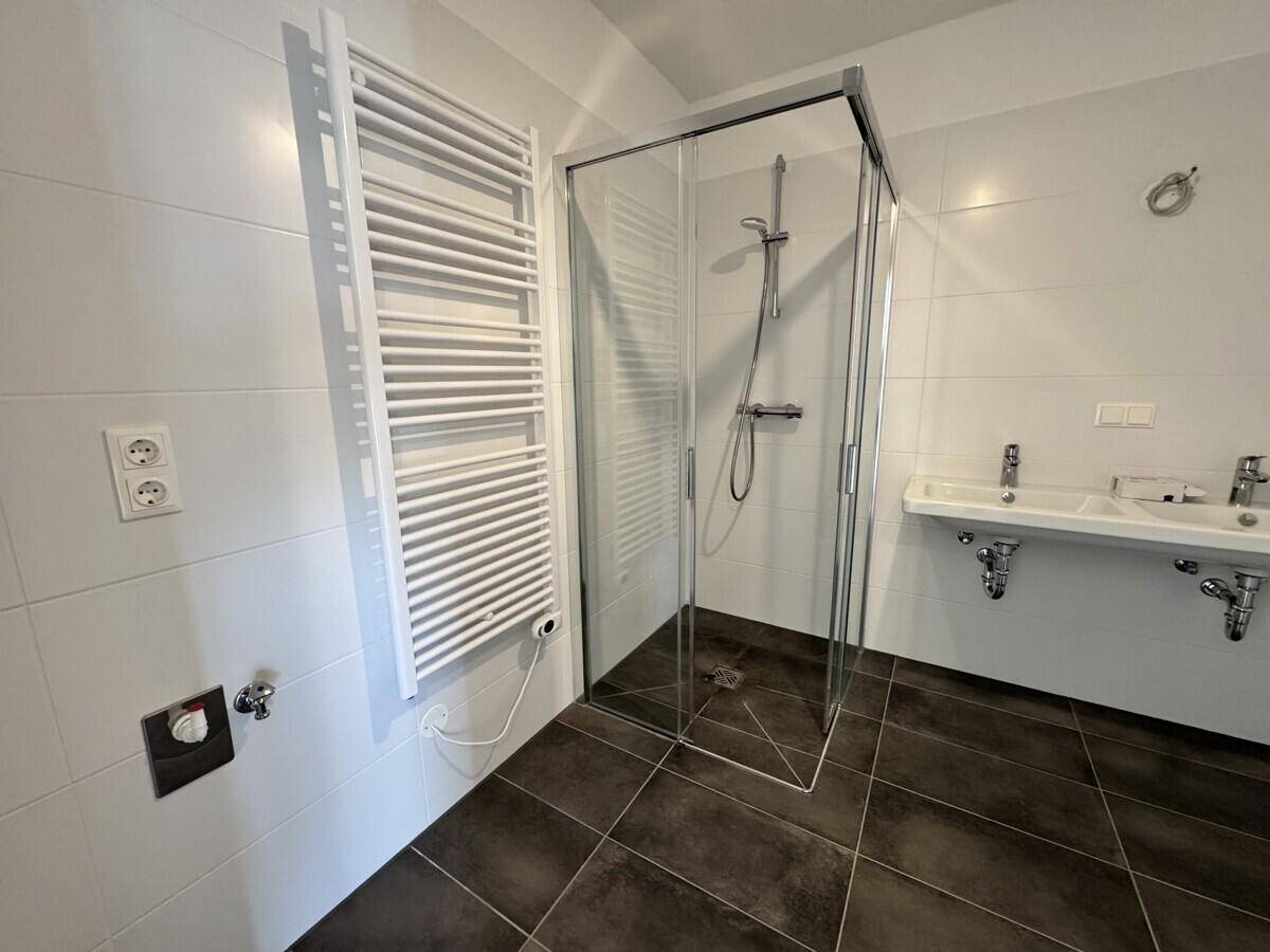 Helles Badezimmer mit Duschkabine, zwei Waschbecken und einem Handtuchheizkörper.