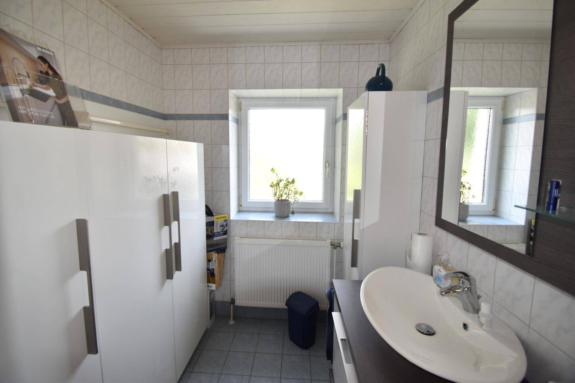 Helles Badezimmer mit Fliesen, Waschbecken, Spiegelschrank und Fenster.