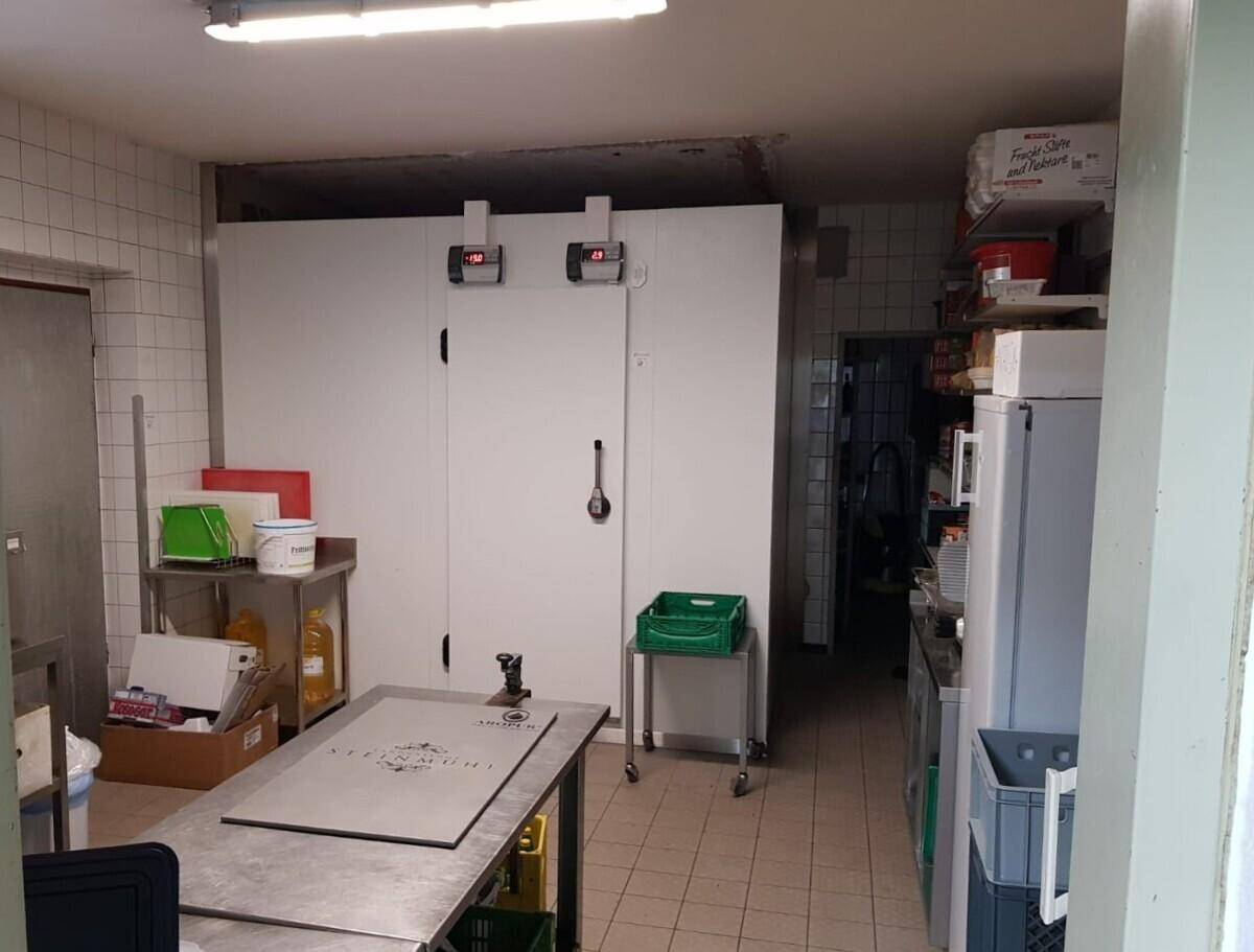 Großküchenbereich mit Kühlzellen, Arbeitsflächen und Lagerregalen für Lebensmittel.