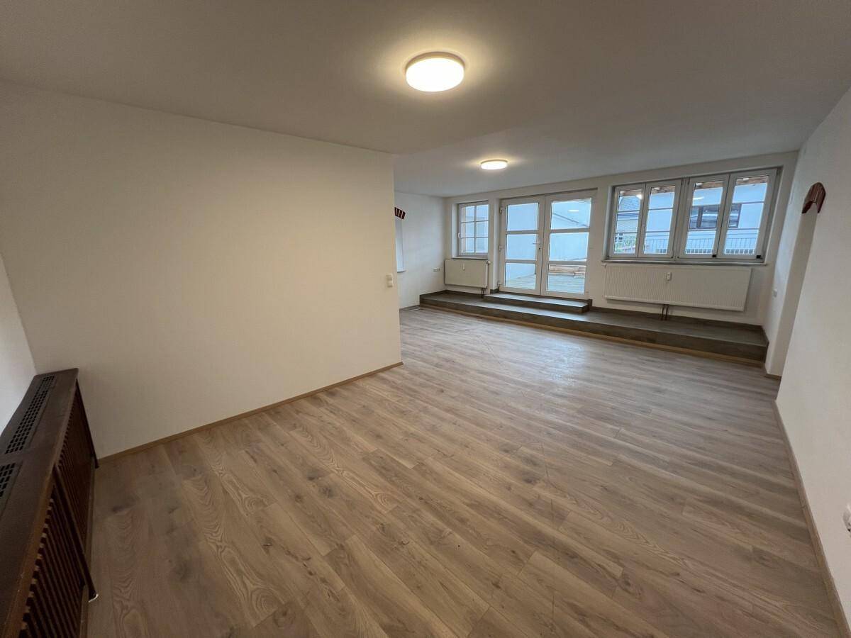 Heller Raum mit Laminatboden und großen Fenstern, die viel Tageslicht hereinlassen.