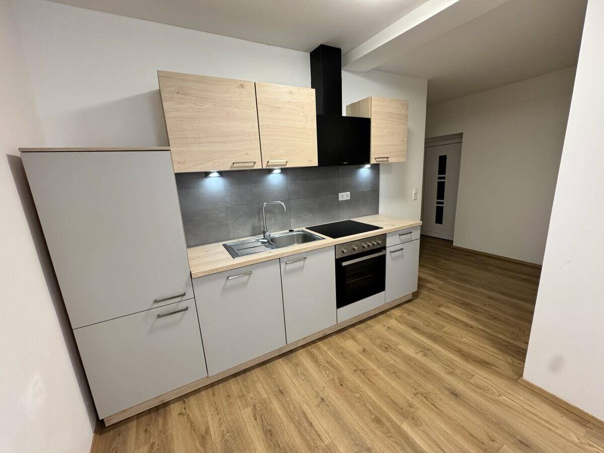 Moderne Einbauküche mit hellen Holzfronten, grauen Unterschränken und integrierten Geräten.