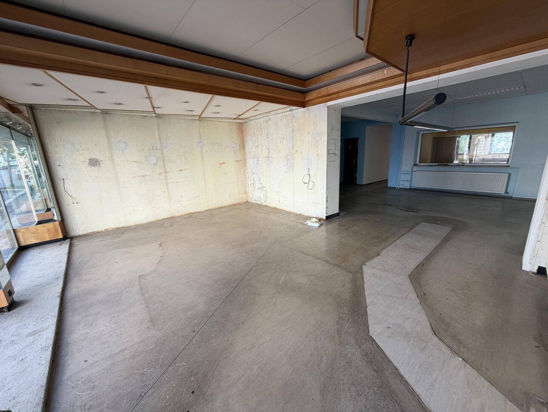 Geräumiger Innenraum mit Holzelementen an der Decke und großen Schaufenstern zur Straße.