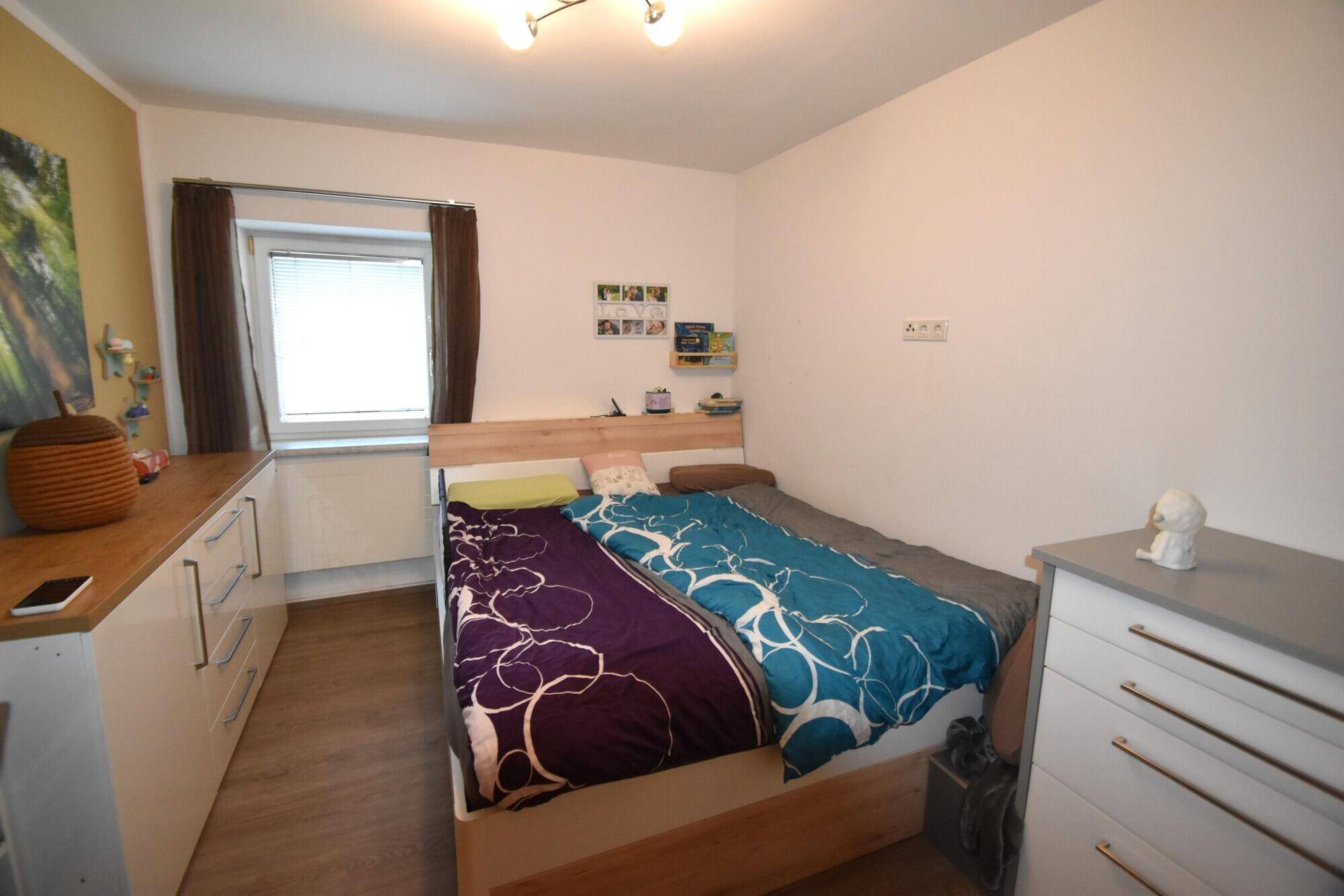 Gemütliches Schlafzimmer mit Holzbett, Kommode und hellem Holzboden.