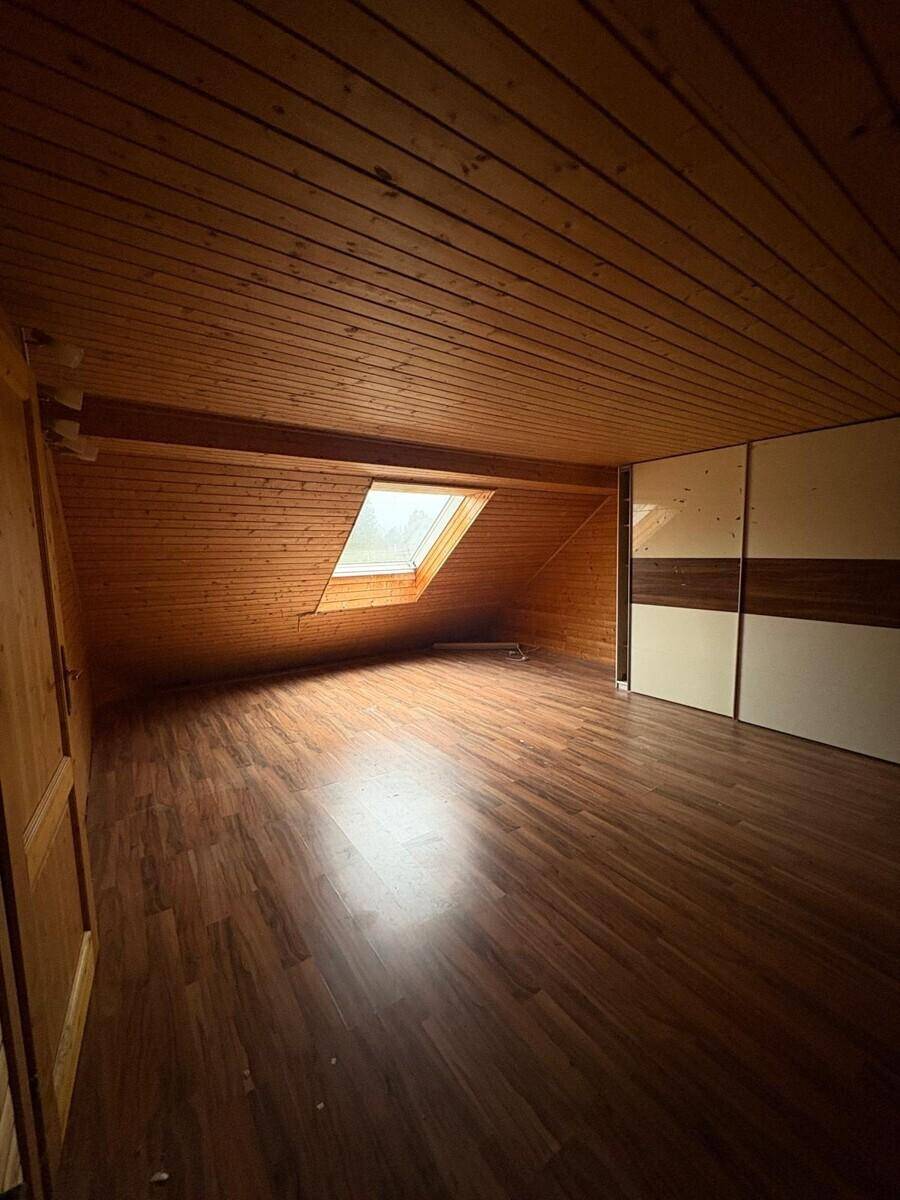 Leeres Schlafzimmer im Dachgeschoss mit Holzvertäfelung, Dachfenster und Laminatboden.