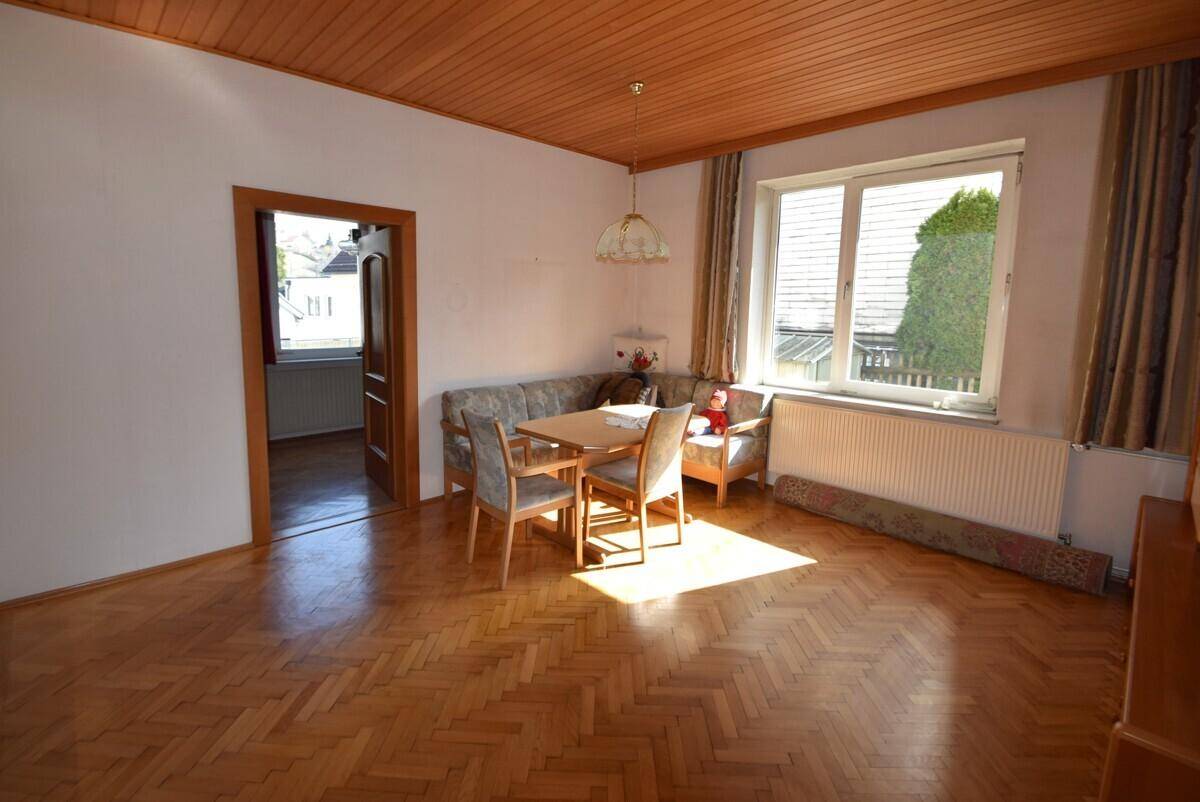 Helles Wohn-Esszimmer mit Fischgrätparkett, Holzdecke und großem Fenster.