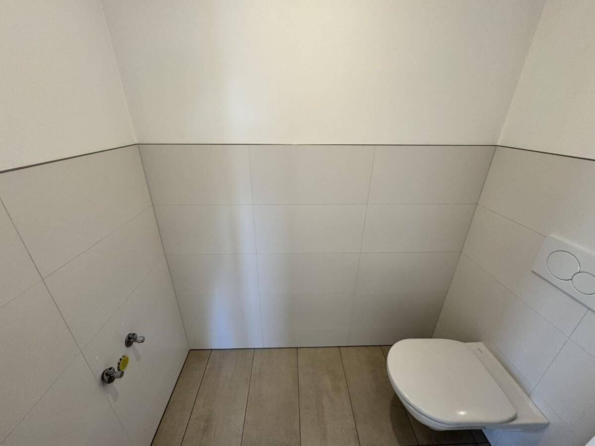 Kleines Gäste-WC mit Wand-WC und halbhohen Fliesen in einem hellen, sauberen Zustand.