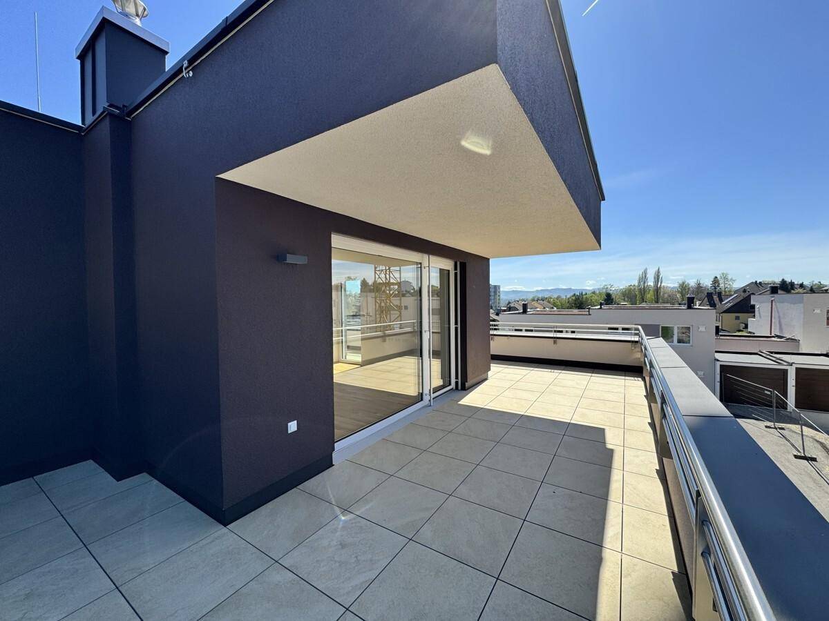 Geräumige Dachterrasse mit Fliesenboden und Blick auf die umliegende Landschaft und Berge.
