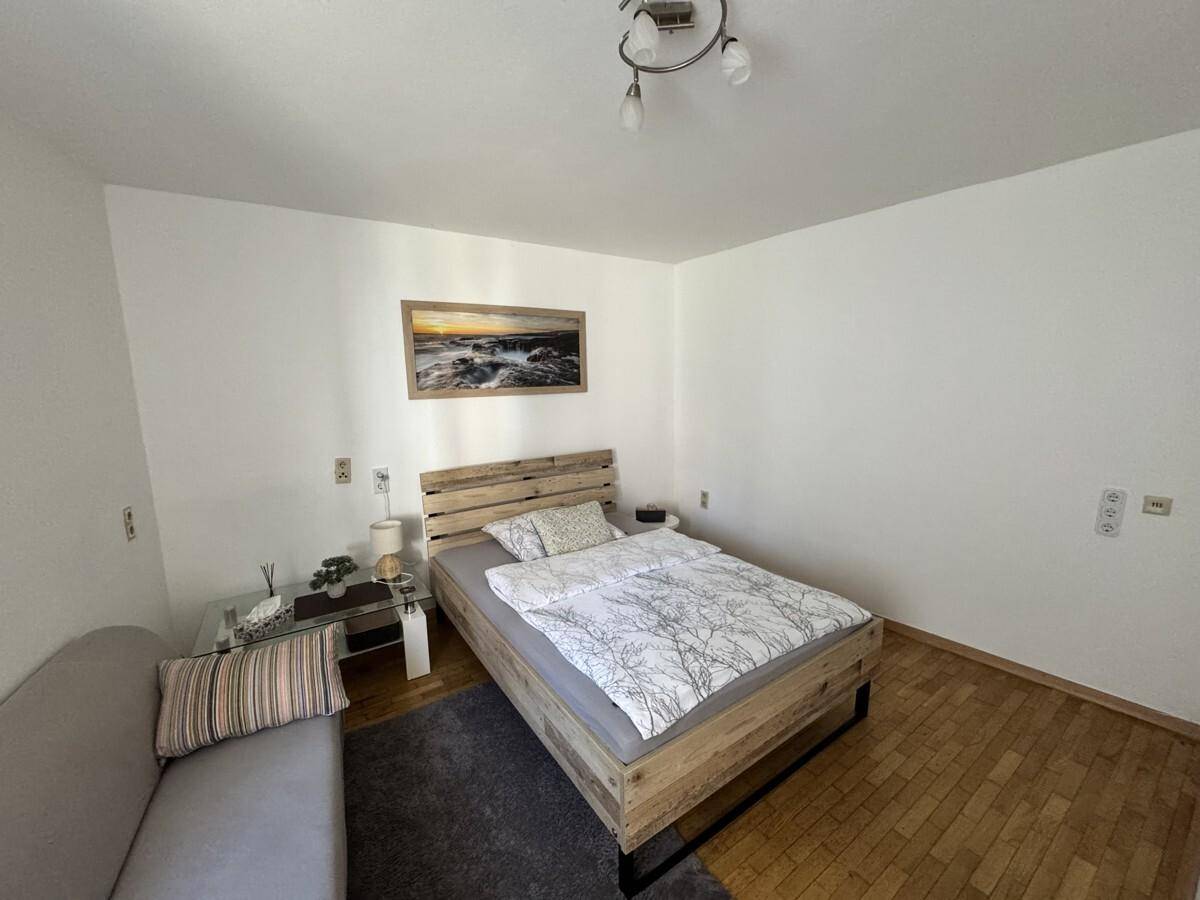 Helles Schlafzimmer mit Doppelbett, Sofa und Holzboden für entspannte Stunden.