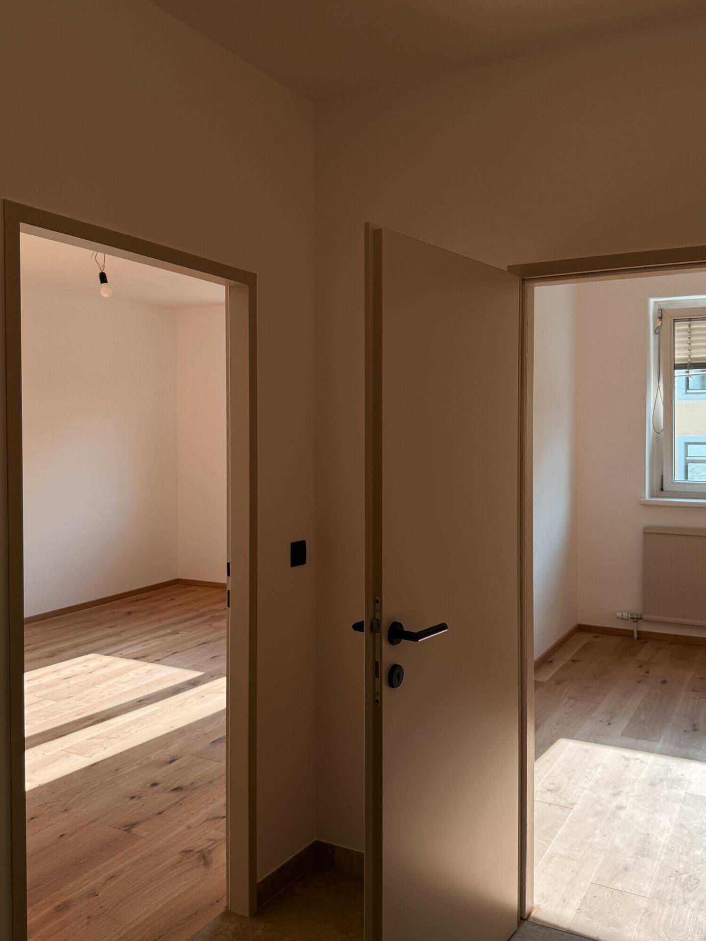 Blick vom Flur in zwei helle Zimmer mit Holzboden und viel Sonnenlicht.