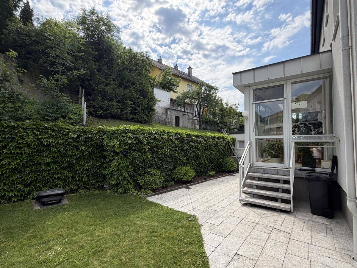 Seitlicher Zugang zum Garten mit gepflastertem Weg und üppiger Heckenbepflanzung.