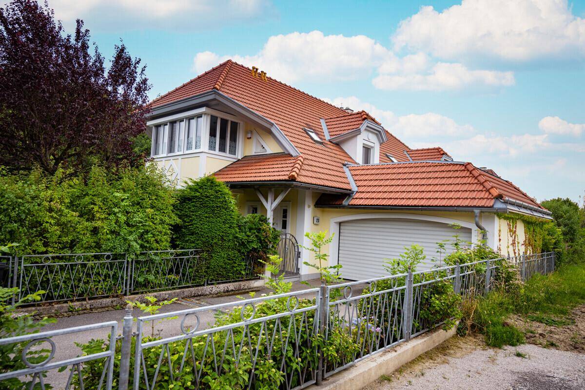 Seitenansicht des Hauses mit Garage, rotem Ziegeldach und üppiger Bepflanzung entlang des Zauns.