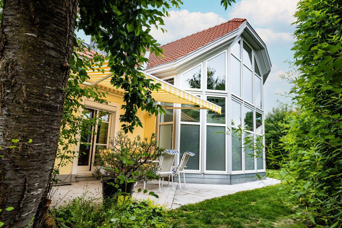 Gemütliche Terrasse mit Gartenmöbeln und Markise neben dem lichtdurchfluteten Wintergarten.