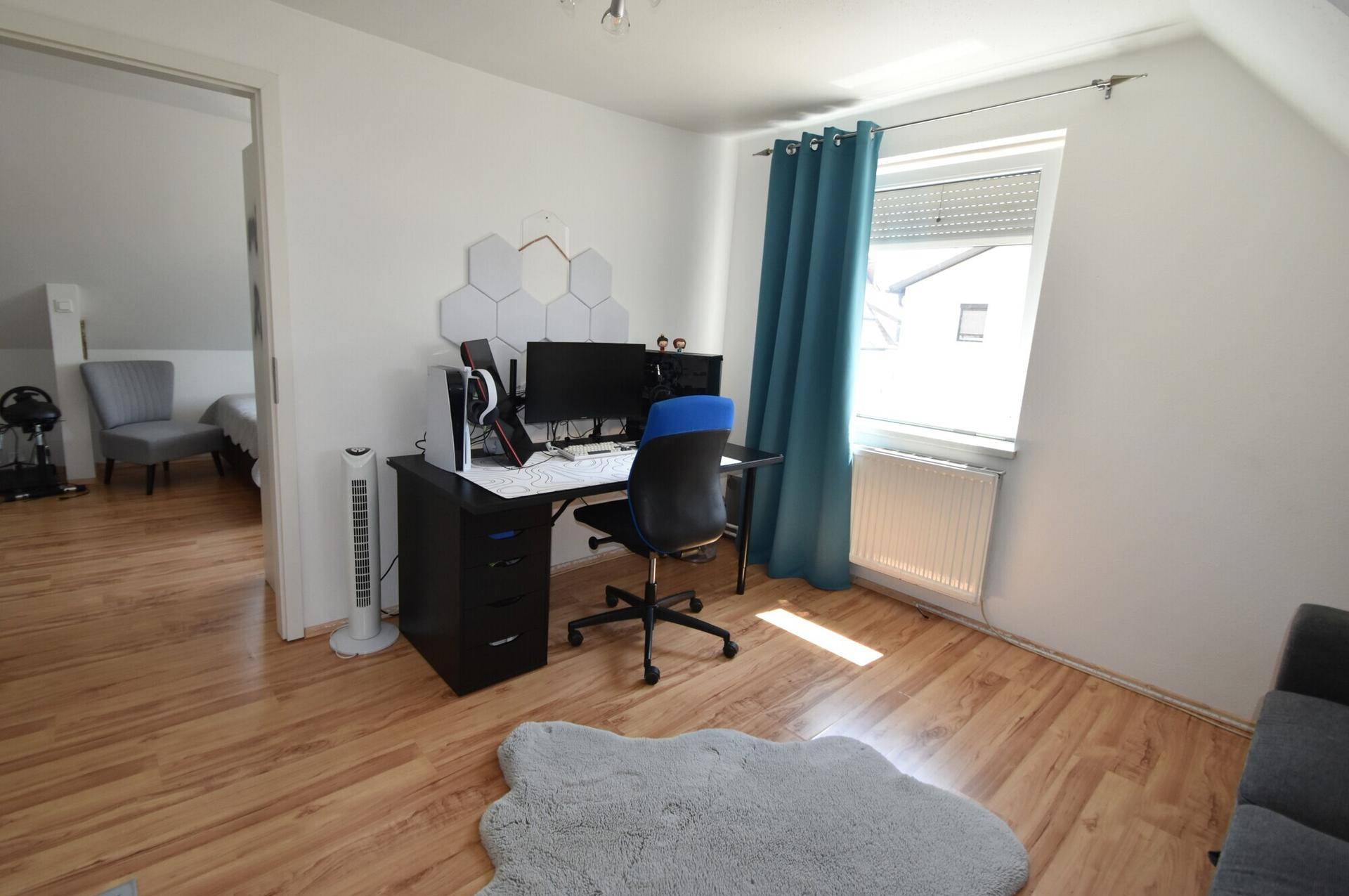 Helles Arbeitszimmer mit Schreibtisch, Computer und Holzboden im Dachgeschoss.