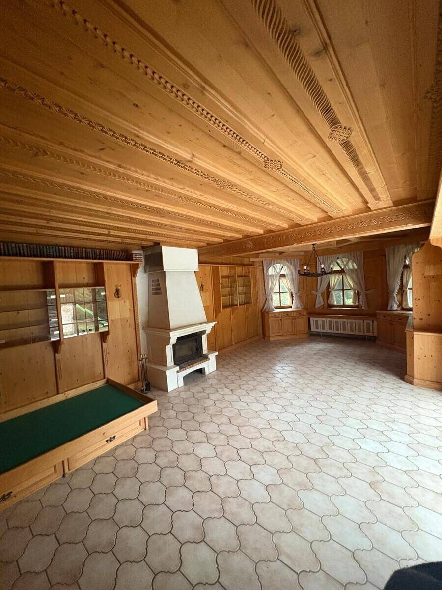 Geräumiger Wohnraum im alpinen Stil mit Holzwänden, Kamin und gemustertem Fliesenboden.