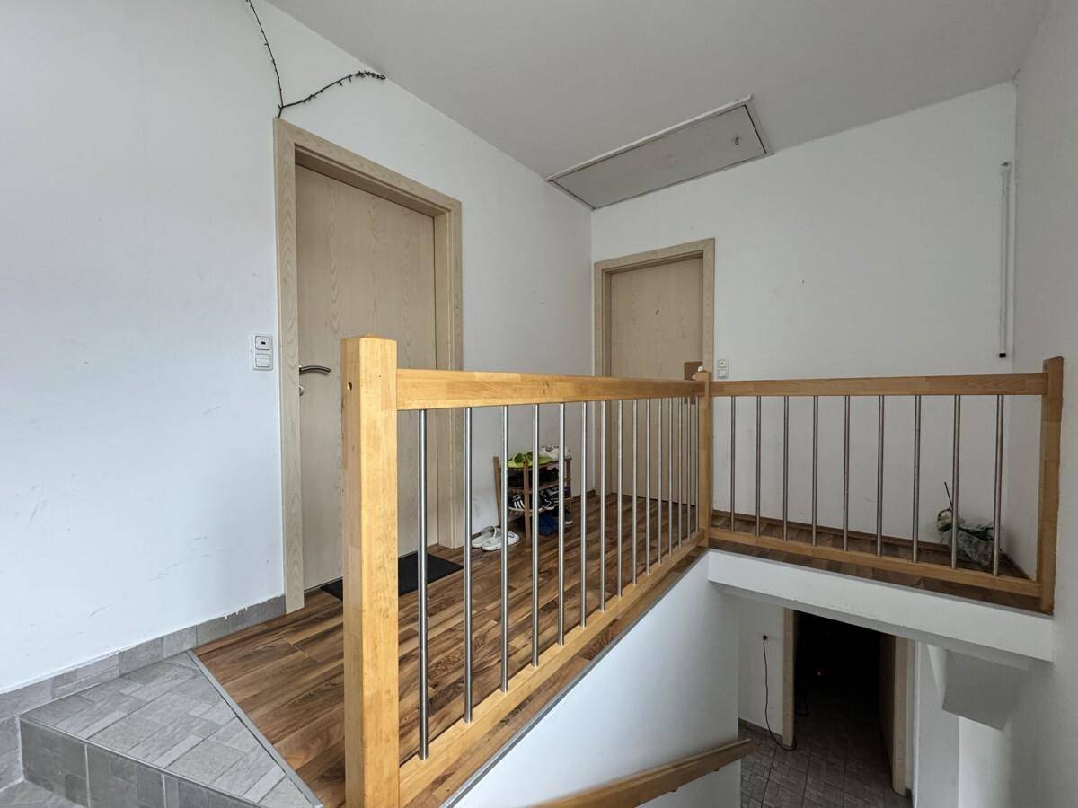 Heller Treppenaufgang mit Holzgeländer und Metallstäben, der zu den Wohnungen führt.