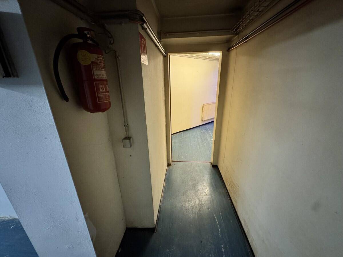 Langer, schmaler Flur im Keller mit blaugrauem Boden und einem Feuerlöscher an der Wand.