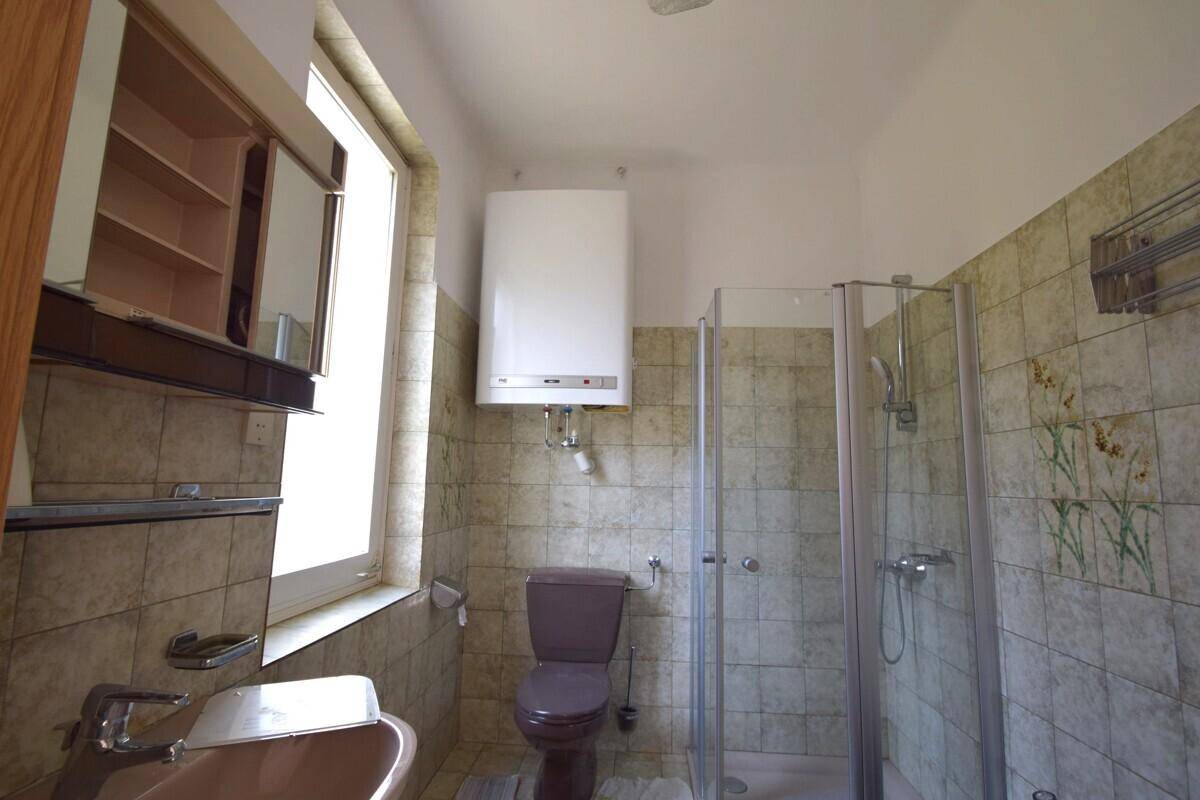 Badezimmer mit Dusche, Fenster und älteren Fliesen in beigem Farbton.