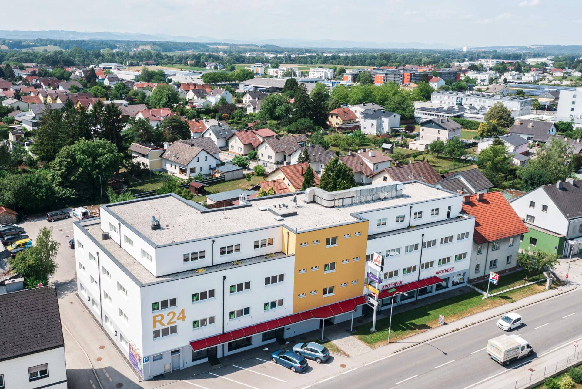 Luftaufnahme des Geschäftsgebäudes mit umliegender Wohnbebauung und grüner Landschaft im Hintergrund.