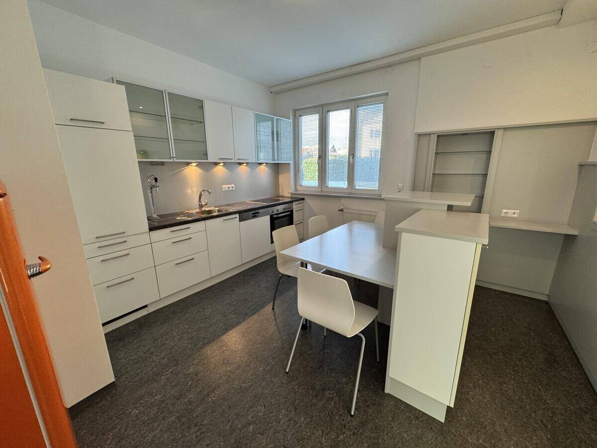 Funktionale Küche mit weißen Schränken, Essbereich und Fenster, ideal für den täglichen Gebrauch.
