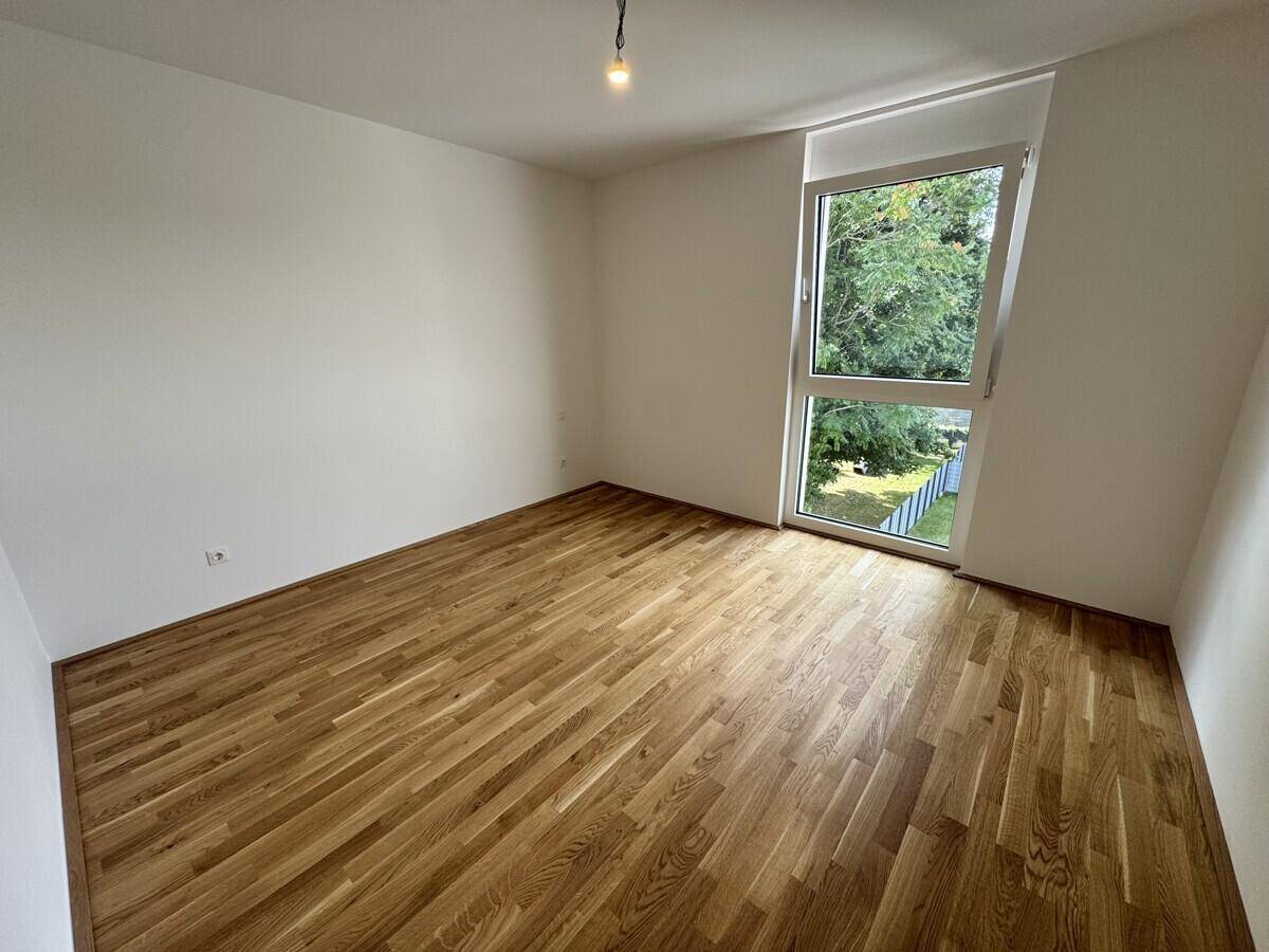 Lichtdurchflutetes Schlafzimmer mit Eichenparkett und Fenster mit Blick ins Grüne.