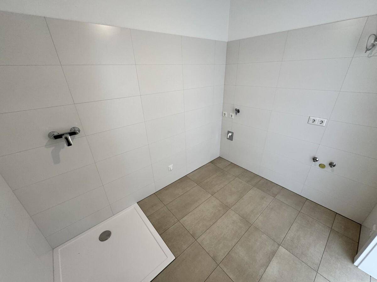 Unfertiges Badezimmer mit Duschbereich, hellen Wandfliesen und Bodenfliesen in neutralem Ton.
