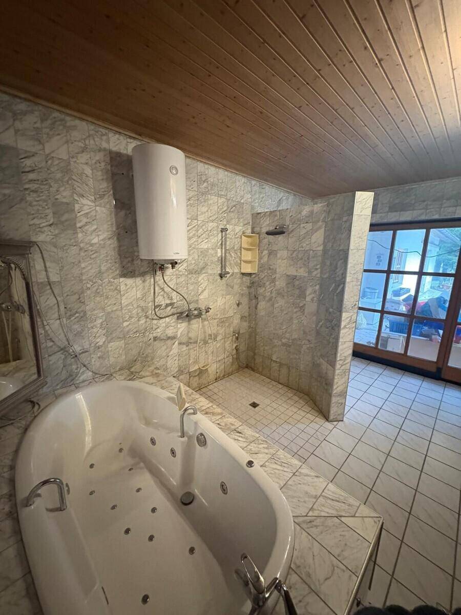 Badezimmer mit Whirlpool-Badewanne, Dusche und Marmorfliesen an den Wänden.