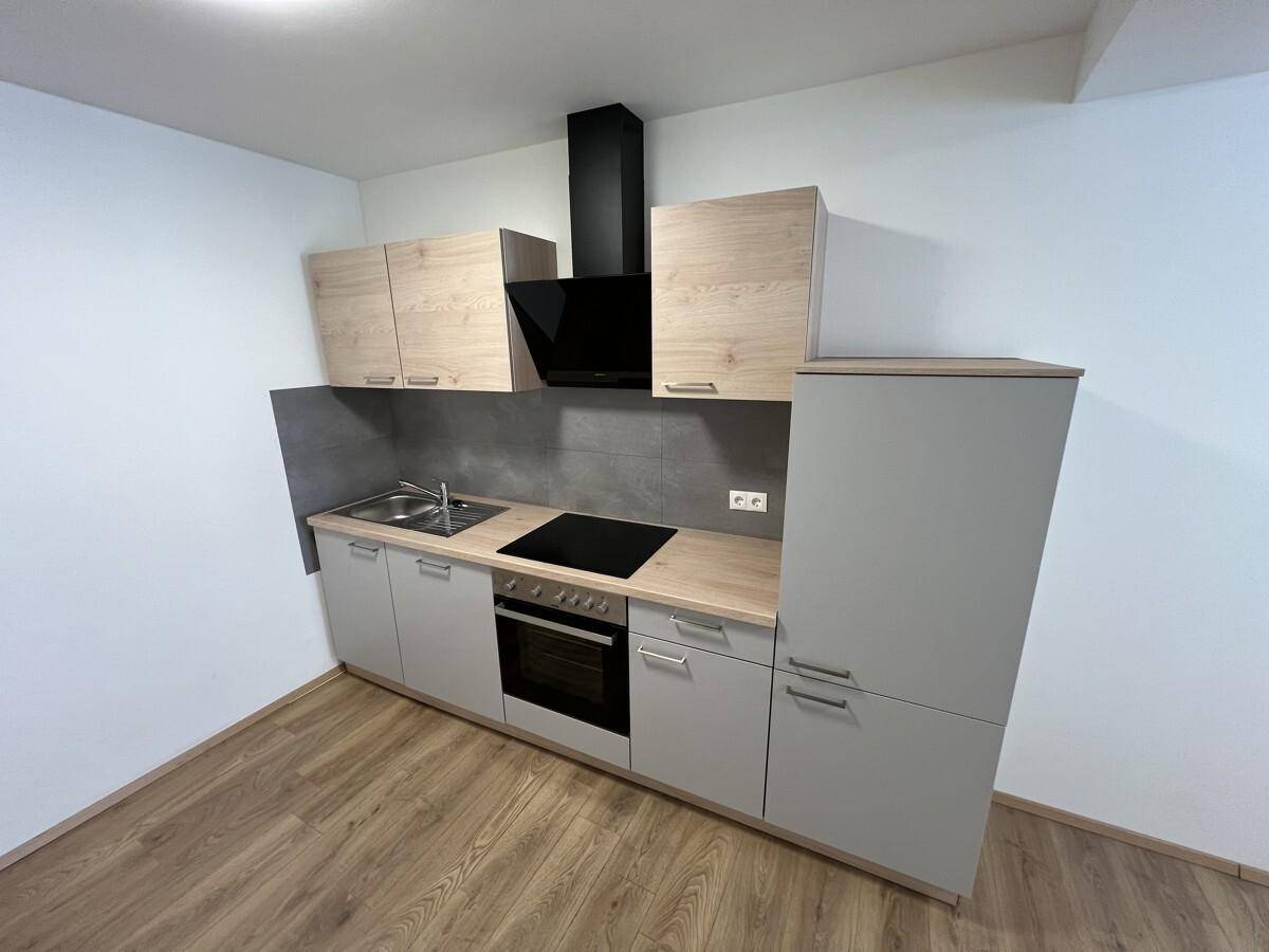 Kompakte Einbauküche mit Holz- und Grautönen, ausgestattet mit Kochfeld und Backofen.