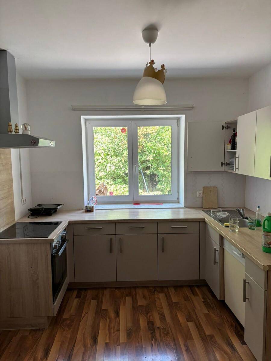 Funktionale Küche mit Holzoptik-Arbeitsplatten, Einbaugeräten und Fenster mit Blick ins Grüne.