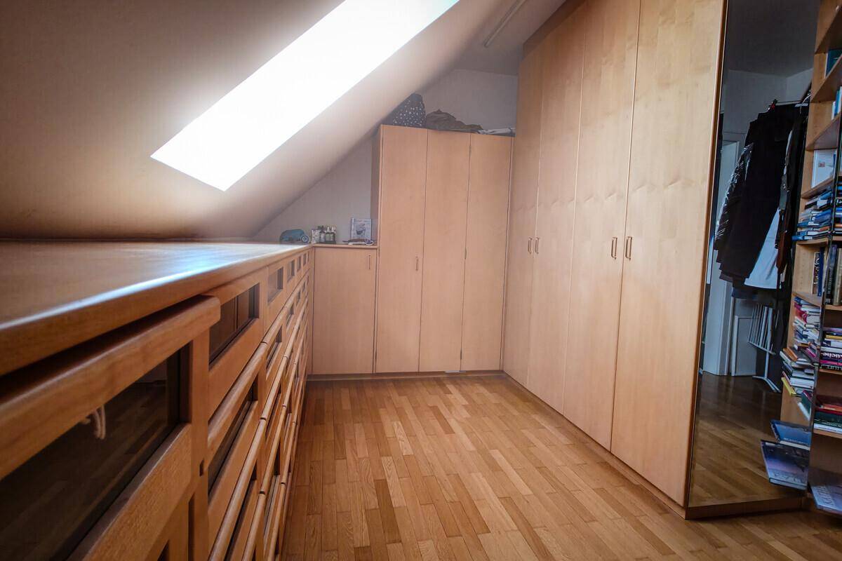 Heller Raum mit Holzschränken, Parkettboden und Dachfenster, ideal als Ankleidezimmer.