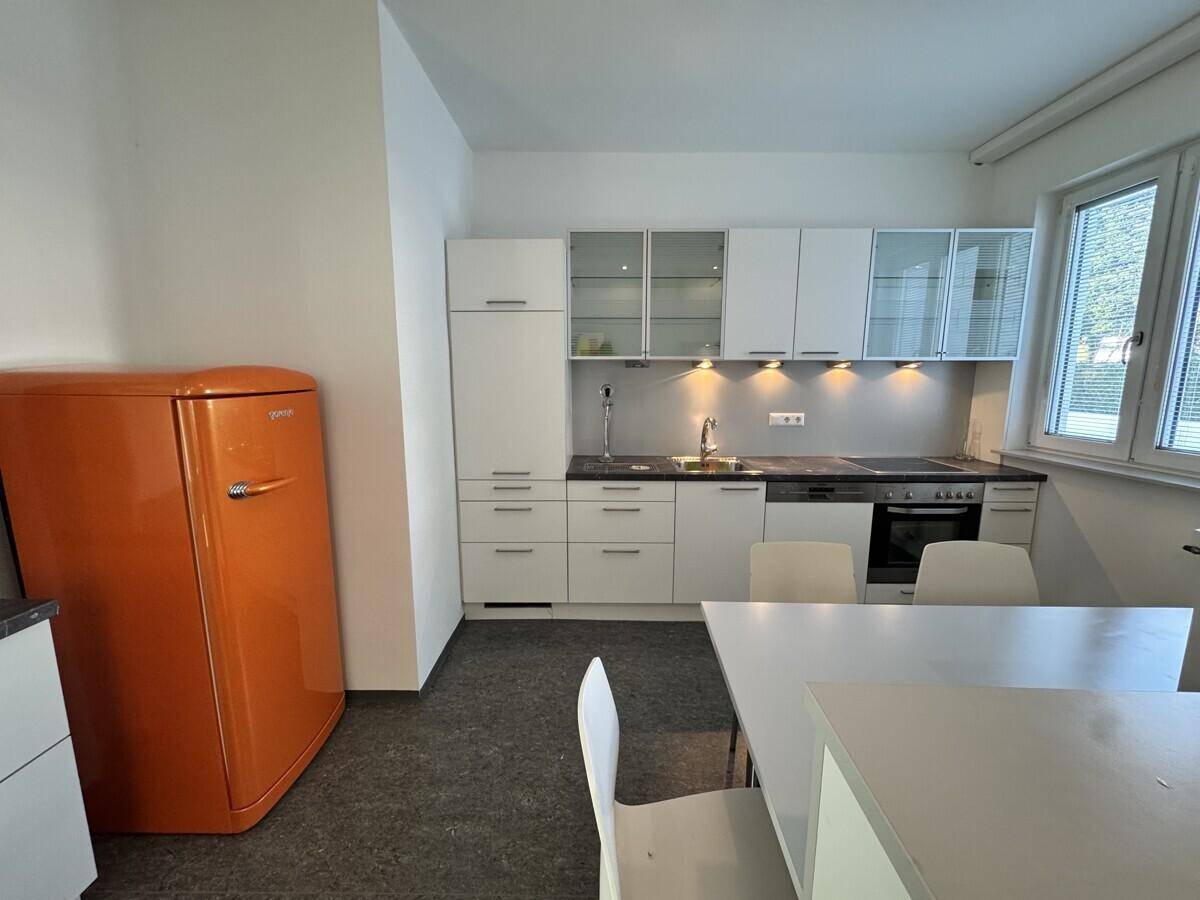 Helle Küche mit weißen Einbauschränken, Essbereich und einem auffälligen orangefarbenen Kühlschrank.