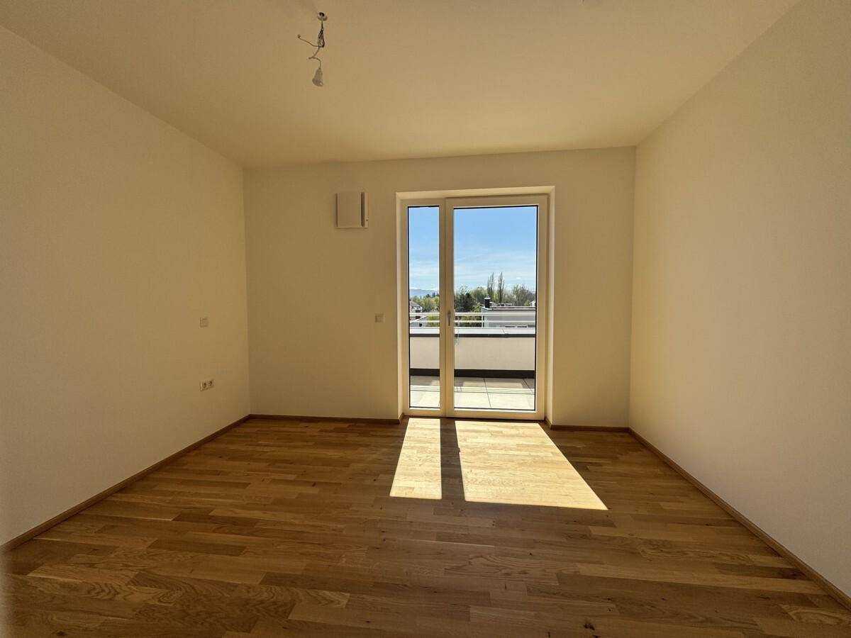 Helles Schlafzimmer mit Holzboden und großem Fenster, das viel Tageslicht hereinlässt.