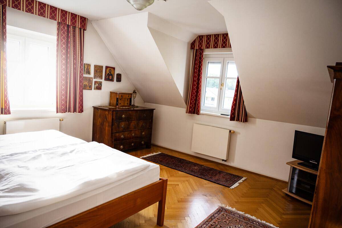 Gemütliches Schlafzimmer im Dachgeschoss mit Holzboden, Dachschrägen und zwei Fenstern.