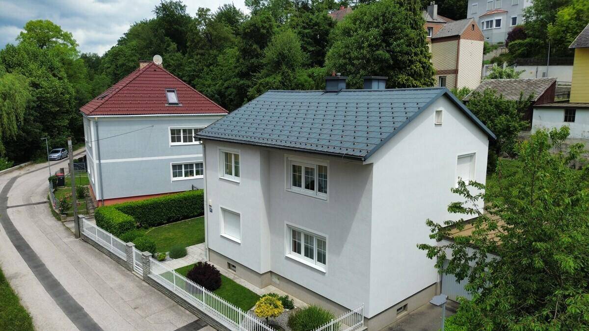 Ansicht eines modernen Einfamilienhauses mit weißer Fassade, großen Fenstern und einem gepflegten Vorgarten.