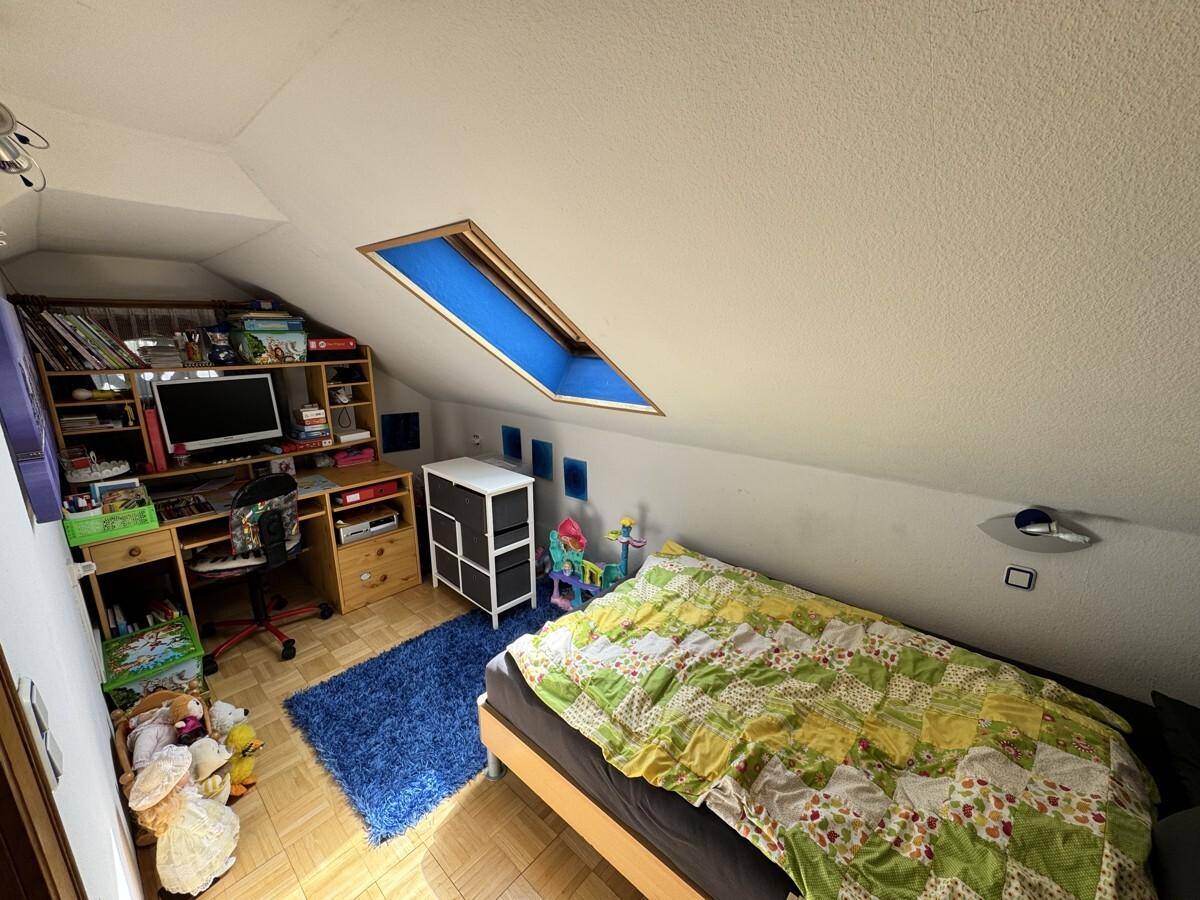 Schlafzimmer im Dachgeschoss mit Dachfenster, Schrägen und Holzboden.