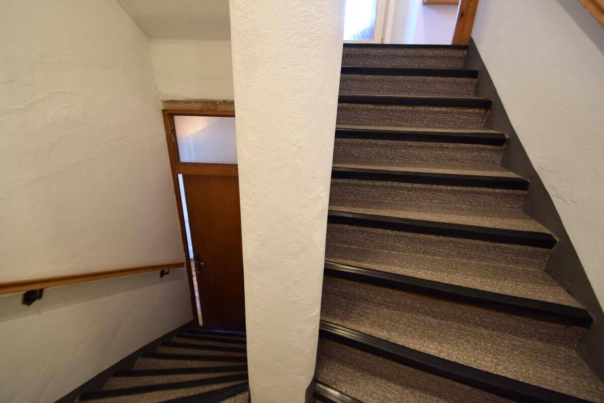 Treppenhaus mit Teppichboden und Holzgeländer, das in die oberen Stockwerke führt.