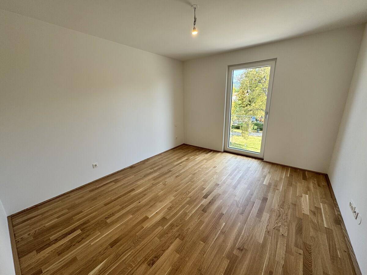 Leeres Schlafzimmer mit hellem Parkettboden und Zugang zu einem potenziellen Balkon oder Garten.
