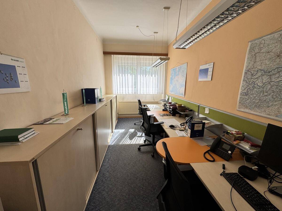 Langer Büroraum mit mehreren Arbeitsplätzen, Teppichboden und praktischen Einbauschränken entlang der Wand.