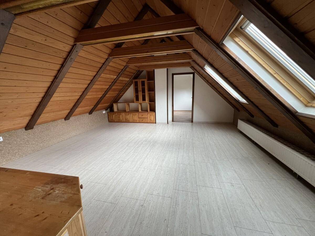 Geräumiger Dachboden mit sichtbaren Holzbalken, Dachfenstern und hellem Boden.