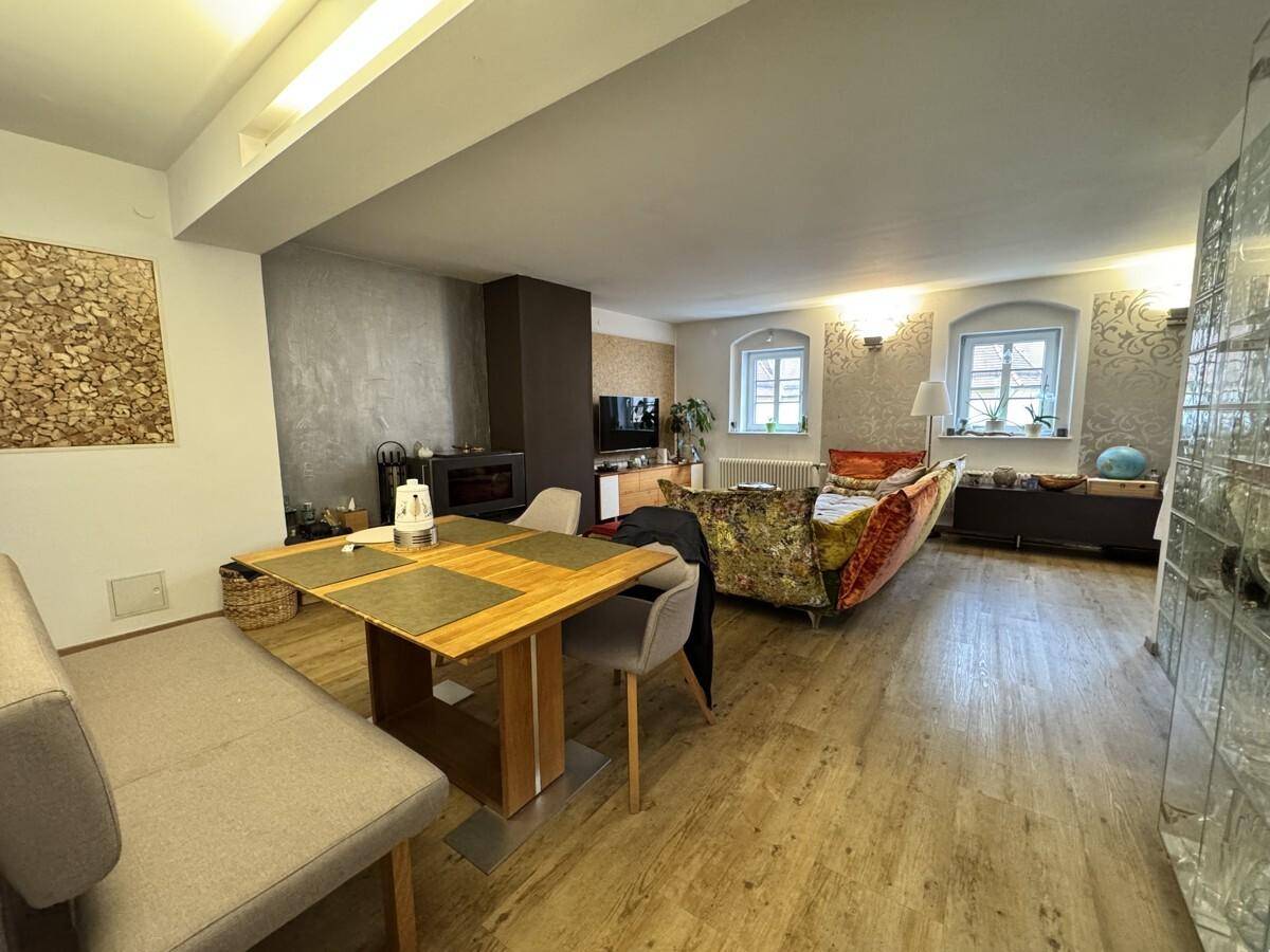 Geräumiger Wohn-Essbereich mit Holzboden, Kamin und einem bunten Sofa.
