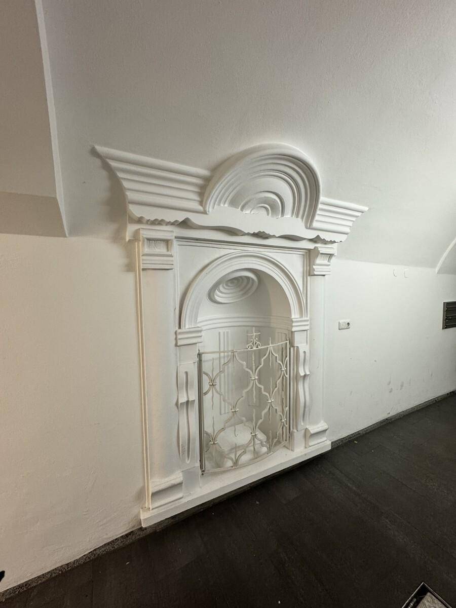 Dekorative Stuckarbeit in einer Nische an der Wand, mit einem verzierten Gitter.