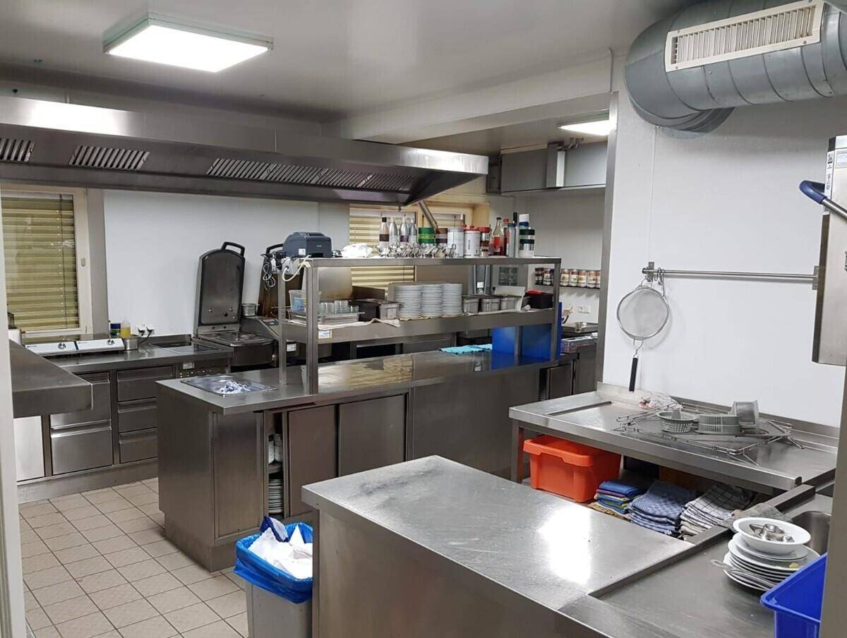 Professionelle Großküche mit Edelstahloberflächen, Abluftsystem und umfangreicher Ausstattung.