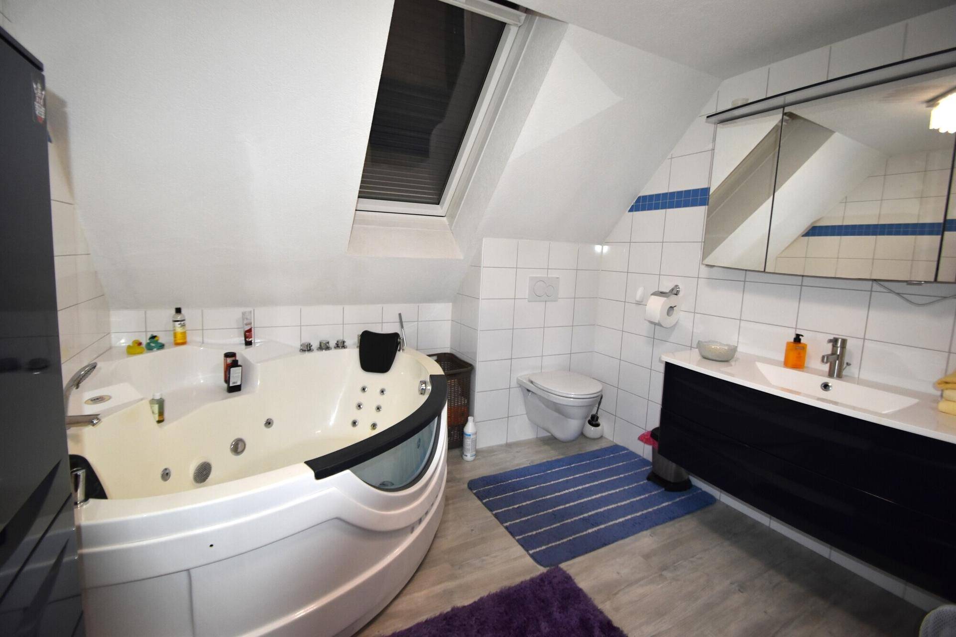 Badezimmer im Dachgeschoss mit Whirlpool-Badewanne, Dachfenster und Waschtisch.